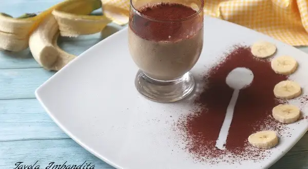 Delizioso dessert al bicchiere con banana e cacao amaro, guarnito con fettine di banana e una spolverata di cacao.