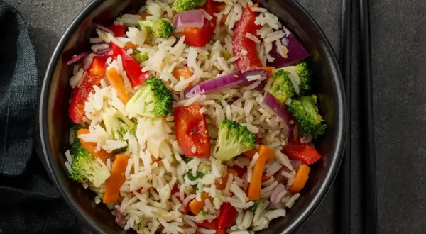 Un piatto colorato di riso con legumi e verdure miste: broccoli, peperoni rossi, carote e cipolla viola.