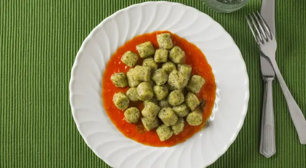 Gnocchi with broccoli in tomato sauce on a white plate, with a fork and knife.