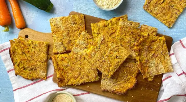 Fette dorate di cecina con verdure, carote e zucchine fresche accanto.