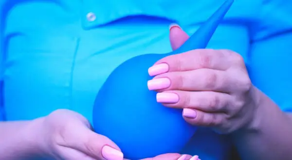 Mani con unghie rosa pastello tengono un clistere blu, pronto per un clistere con acqua del rubinetto.