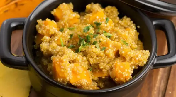 Un saporito piatto di quinoa e zucca, guarnito con erbe fresche, servito in una ciotola nera.