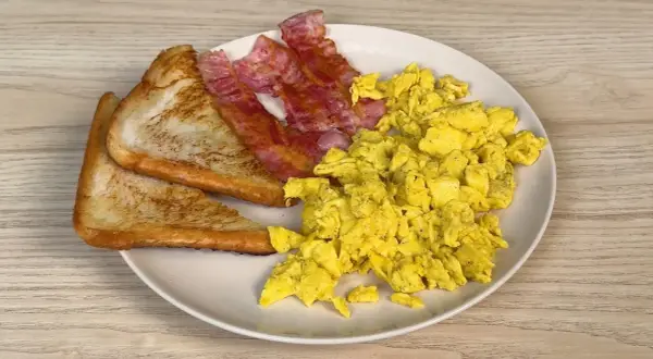 Piatto con uova strapazzate, bacon croccante e pane tostato. Un classico per iniziare la giornata con gusto.