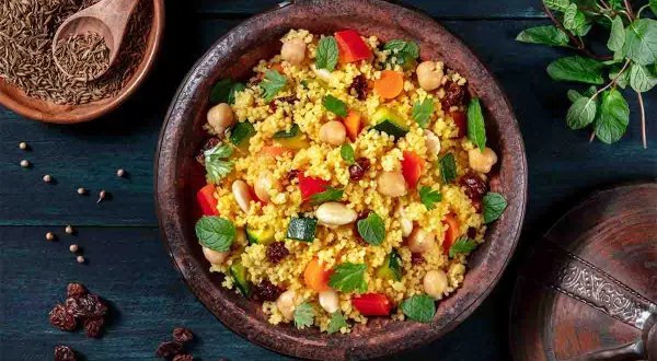 Un piatto colorato di cous cous, con ceci, verdure e uvetta, che evoca le sue antiche origini.