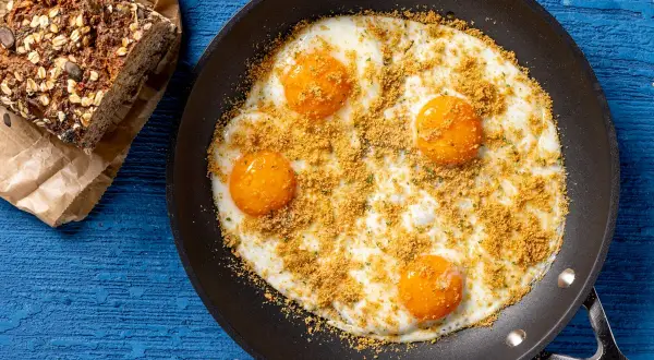 Uova fritte in padella con pangrattato e erbe, accompagnate da pane integrale. Un'idea per ricette fit con uova, sana e gustosa.