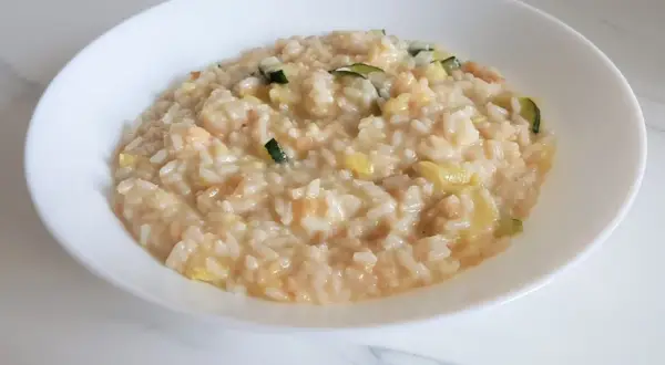 Un cremoso risotto con verdure light, arricchito da zucchine e altri ortaggi freschi, servito in una ciotola bianca.