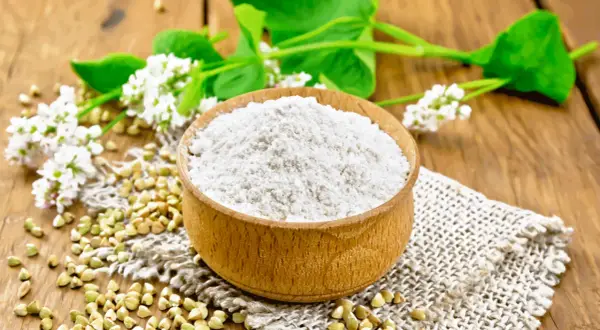Farina di grano saraceno in ciotola, chicchi e fiori. Un alimento utile per chi soffre di colon irritabile.