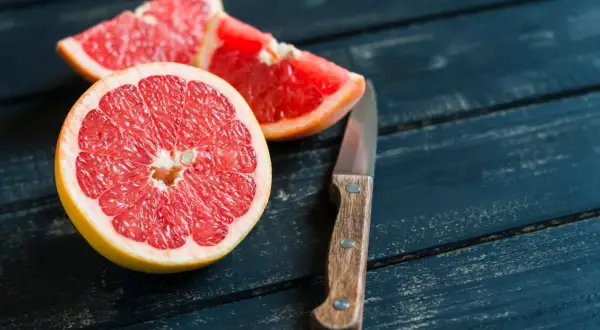 Mezzo pompelmo succoso e spicchi su un tavolo di legno scuro, pronti per essere gustati a stomaco vuoto.