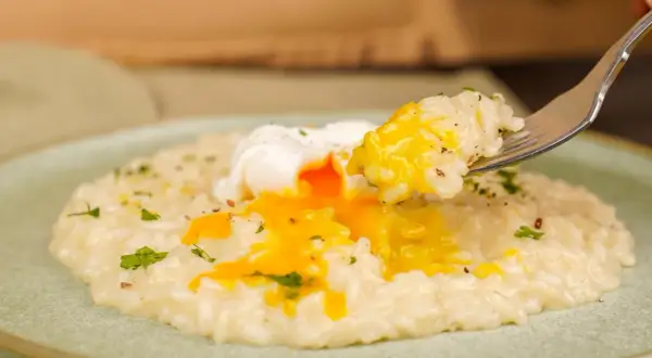 Un piatto di riso in bianco cremoso con un uovo in camicia dal tuorlo dorato che cola. Una forchettata di riso e uovo pronta per essere gustata.