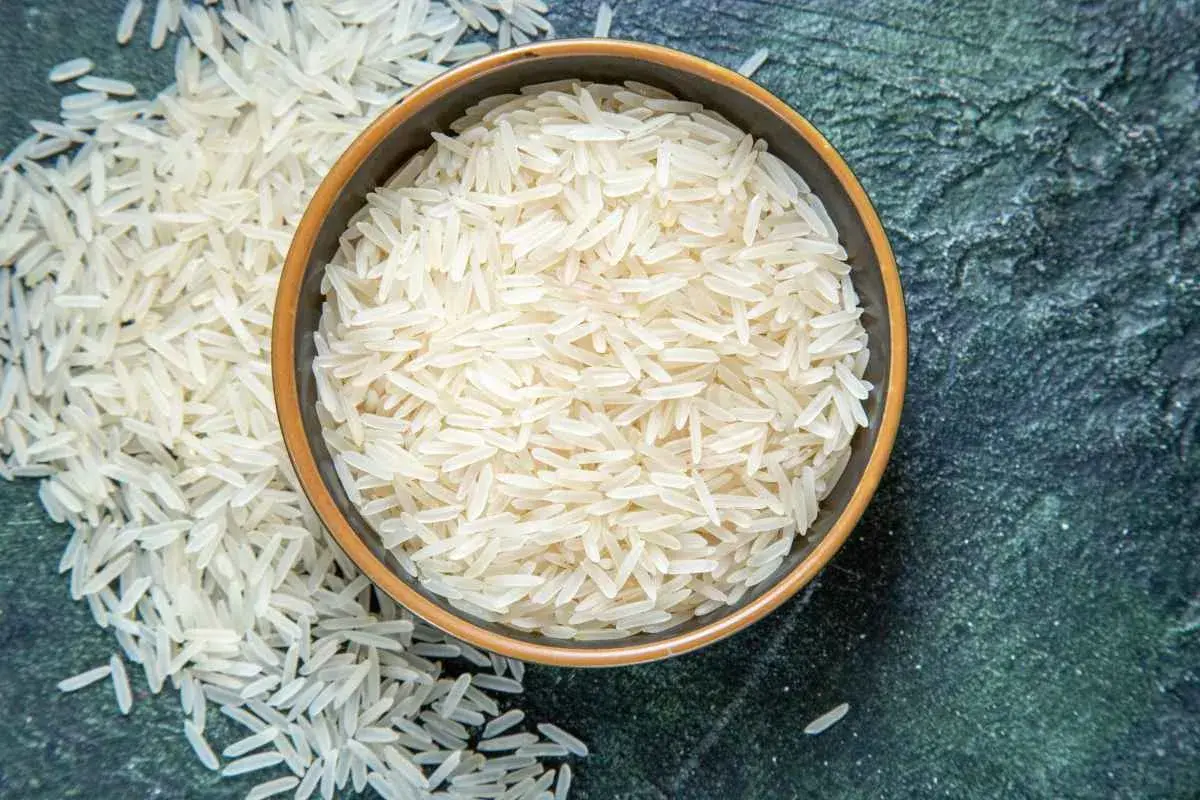 Chicchi di riso basmati in una ciotola e sparsi su una superficie scura. Il riso è noto per le sue proprietà nutritive e versatilità in cucina.