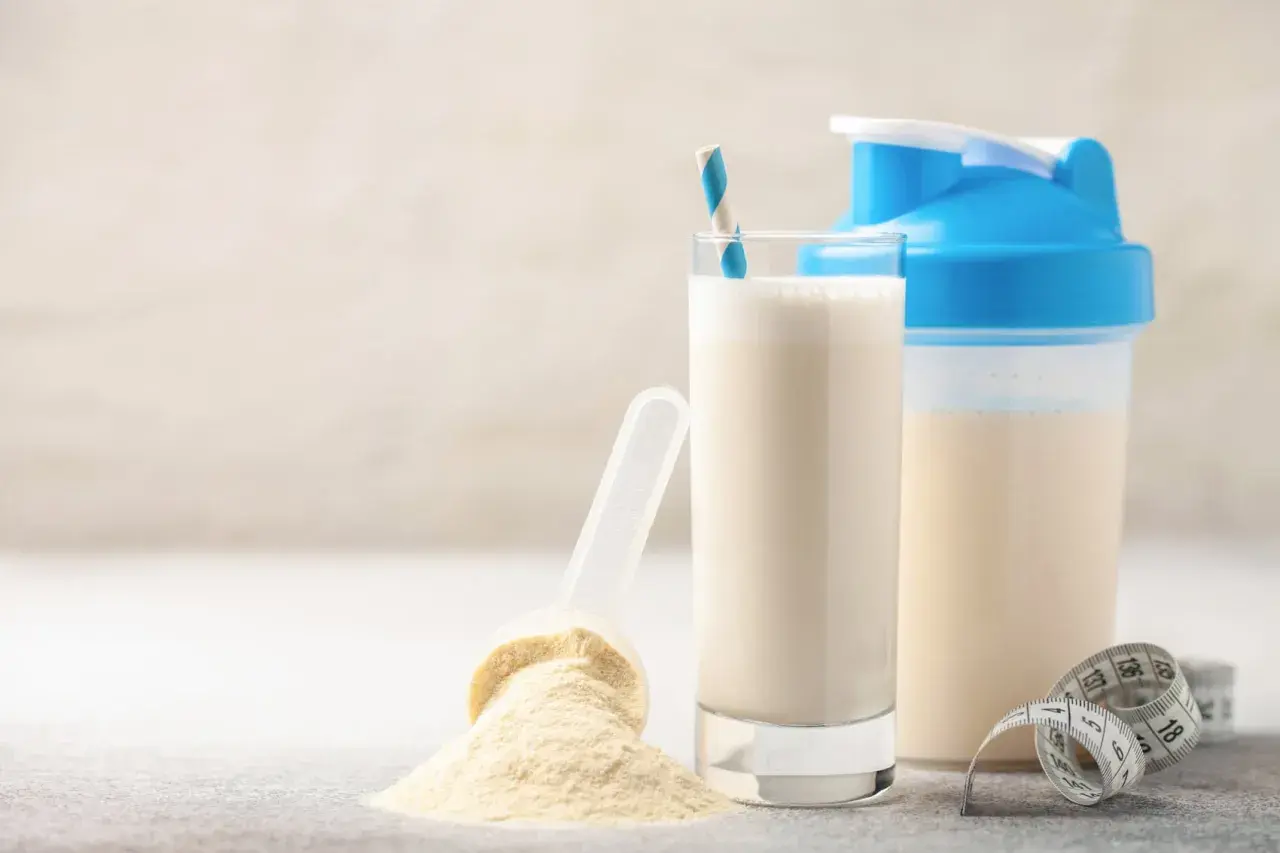 Un bicchiere di latte, una paletta con polvere proteica e uno shaker. Alcuni pensano che il siero del latte fa male, ma è un integratore comune.