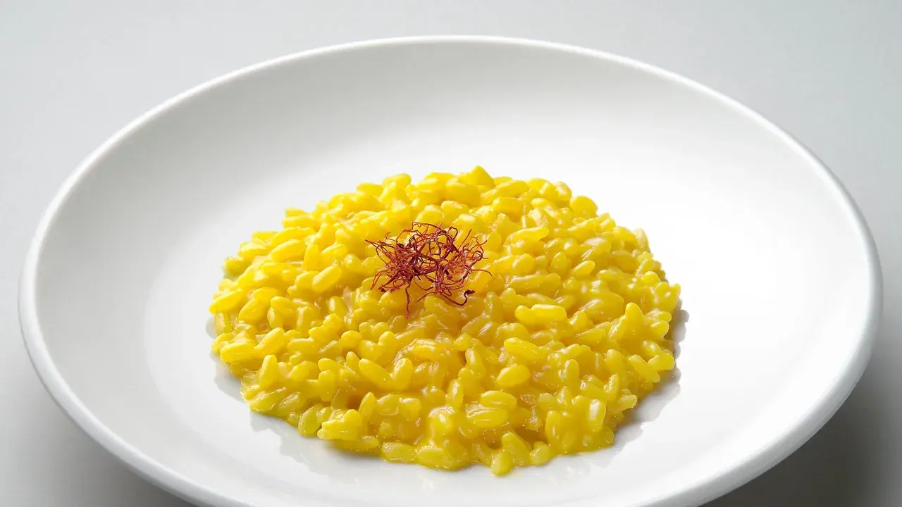 Un cremoso risotto giallo zafferano, guarnito con fili di zafferano, un piatto che promette un riso più leggero e gustoso.