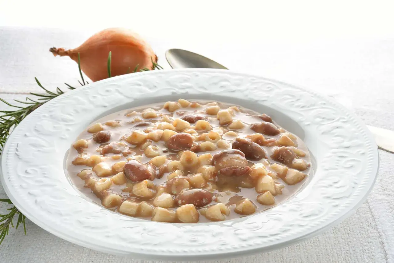 Piatto di pasta e fagioli borlotti, con cipolla e rosmarino sullo sfondo. Un comfort food che scalda il cuore.
