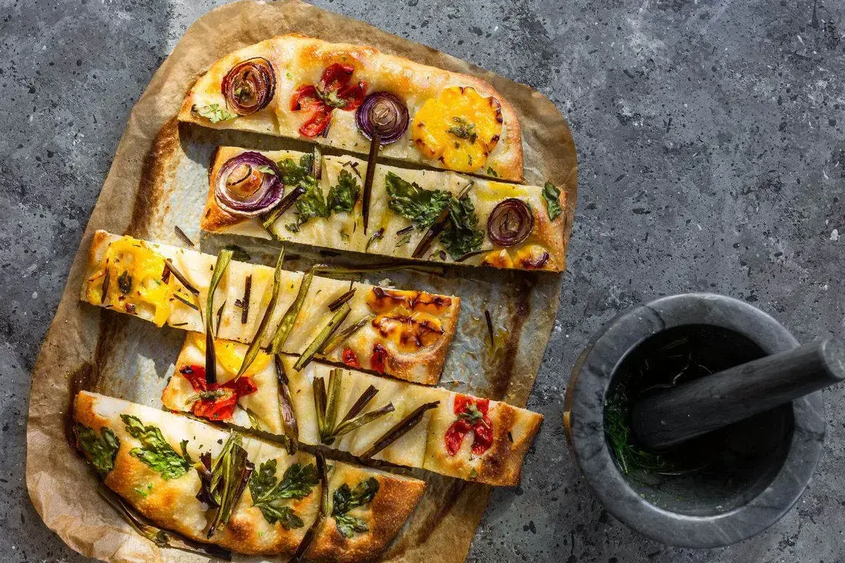Focaccia di verdure colorata con cipolle rosse, pomodorini e erbe aromatiche, pronta per essere gustata.