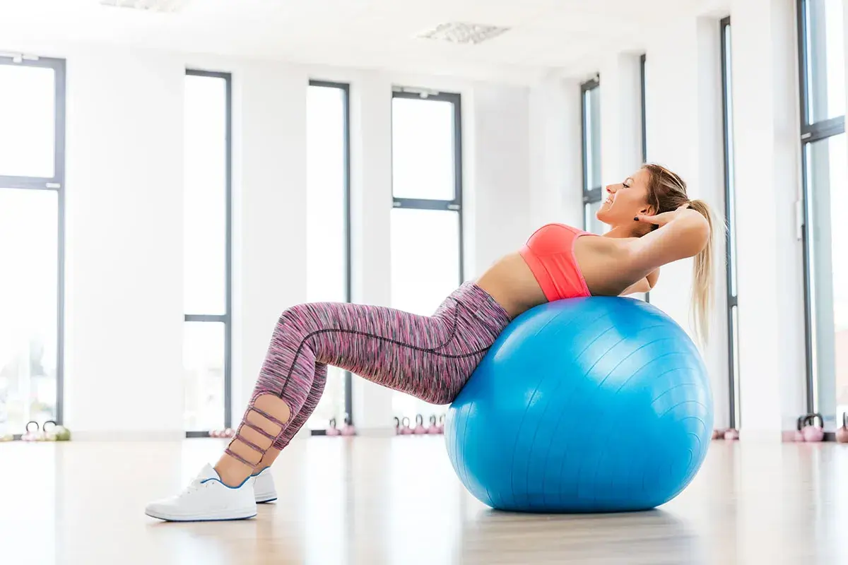 Donna sorridente esegue crunch su palla fitness, parte di esercizi con la palla per dimagrire.