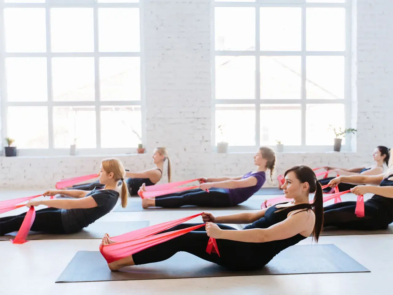 Donne in posa pilates con elastici rossi, un allenamento efficace per chi vuole che il pilates fa dimagrire.