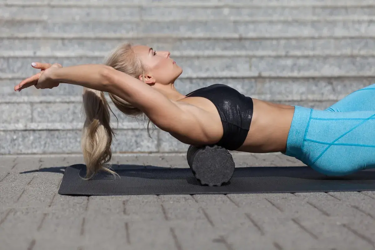 Donna bionda usa un foam roller schiena per rilassare i muscoli dopo l'allenamento.