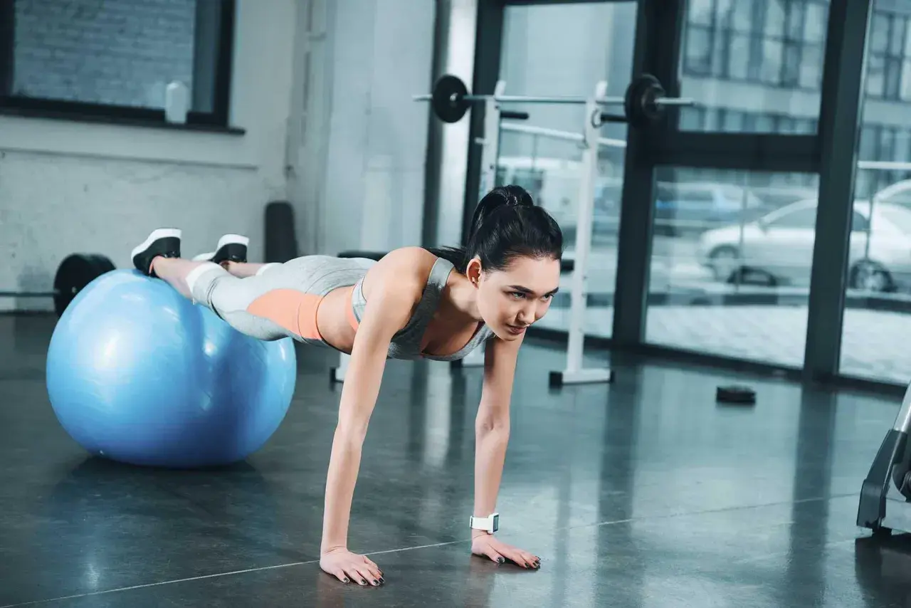 Donna esegue addominali con la palla, mantenendo la posizione plank con i piedi appoggiati sulla palla svizzera blu.