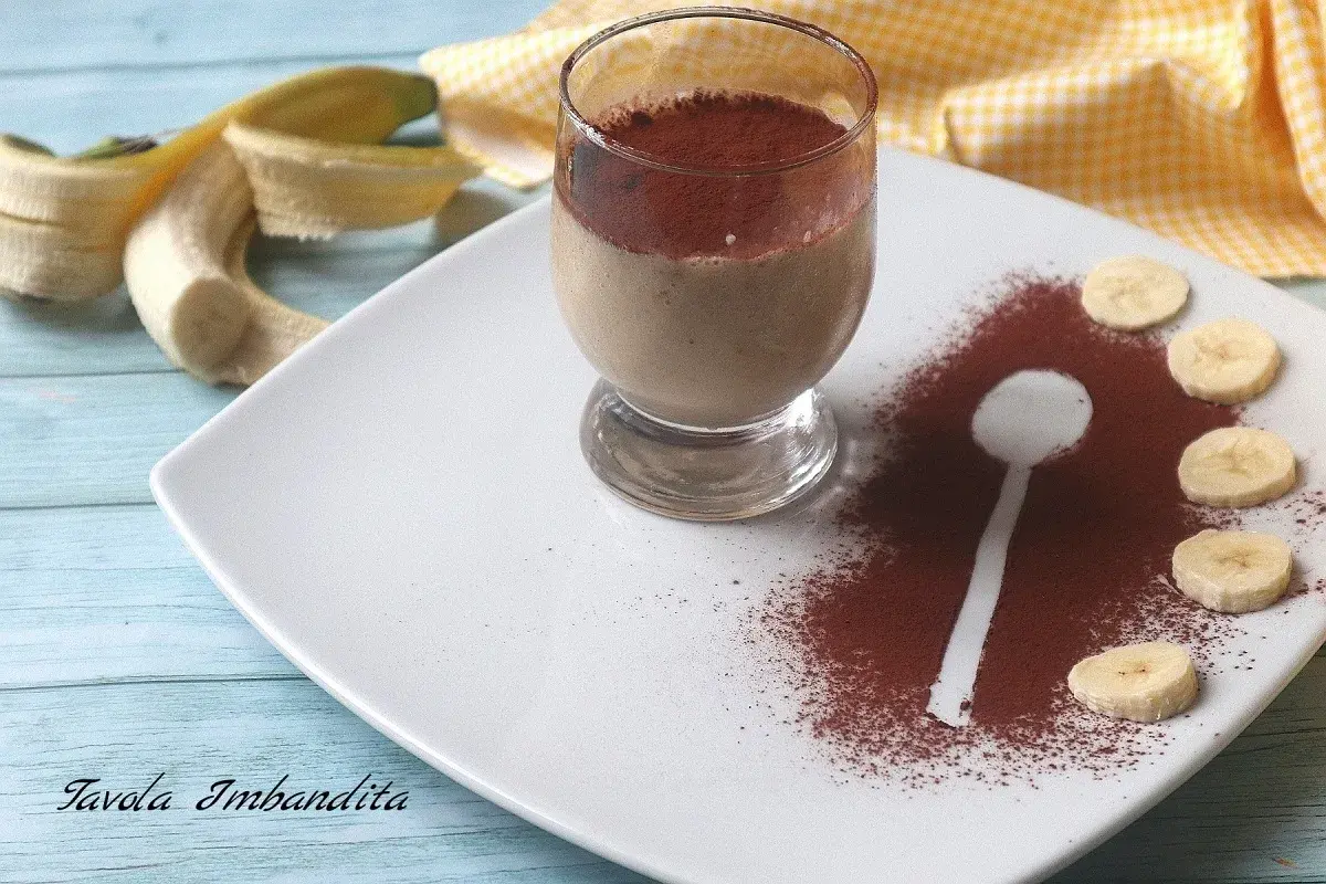 Delizioso dessert al bicchiere con banana e cacao amaro, guarnito con fettine di banana e una spolverata di cacao.