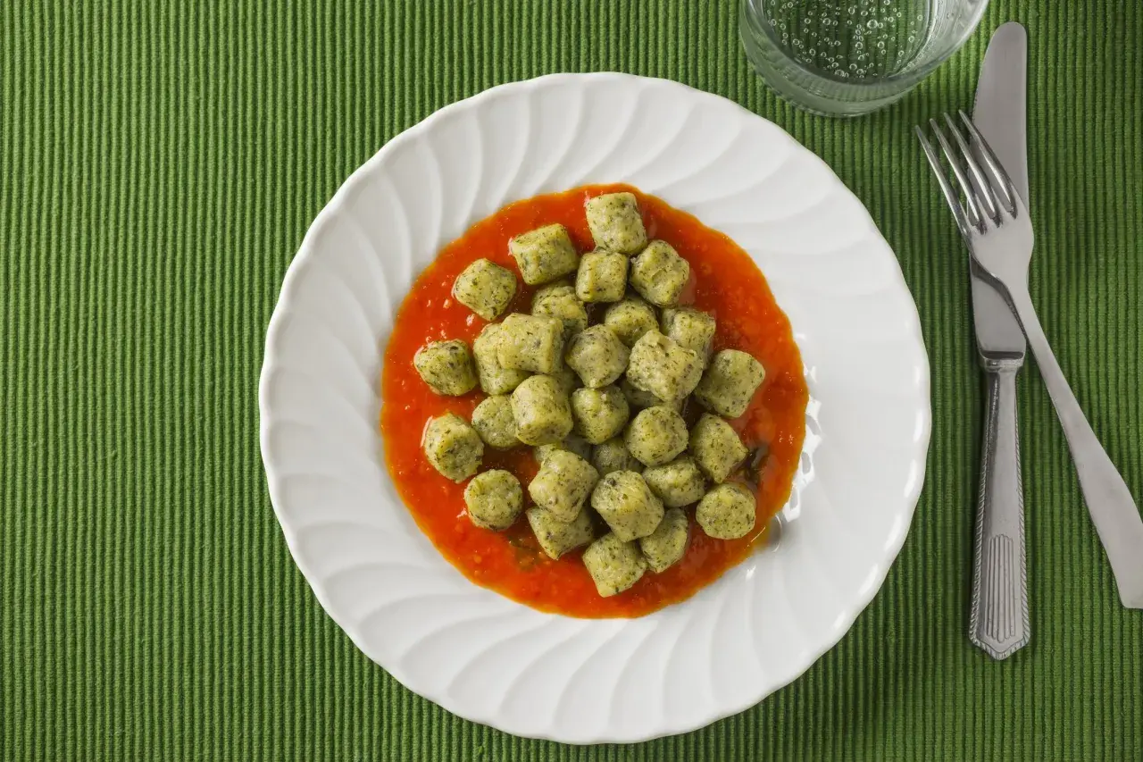 Gnocchi with broccoli in tomato sauce on a white plate, with a fork and knife.