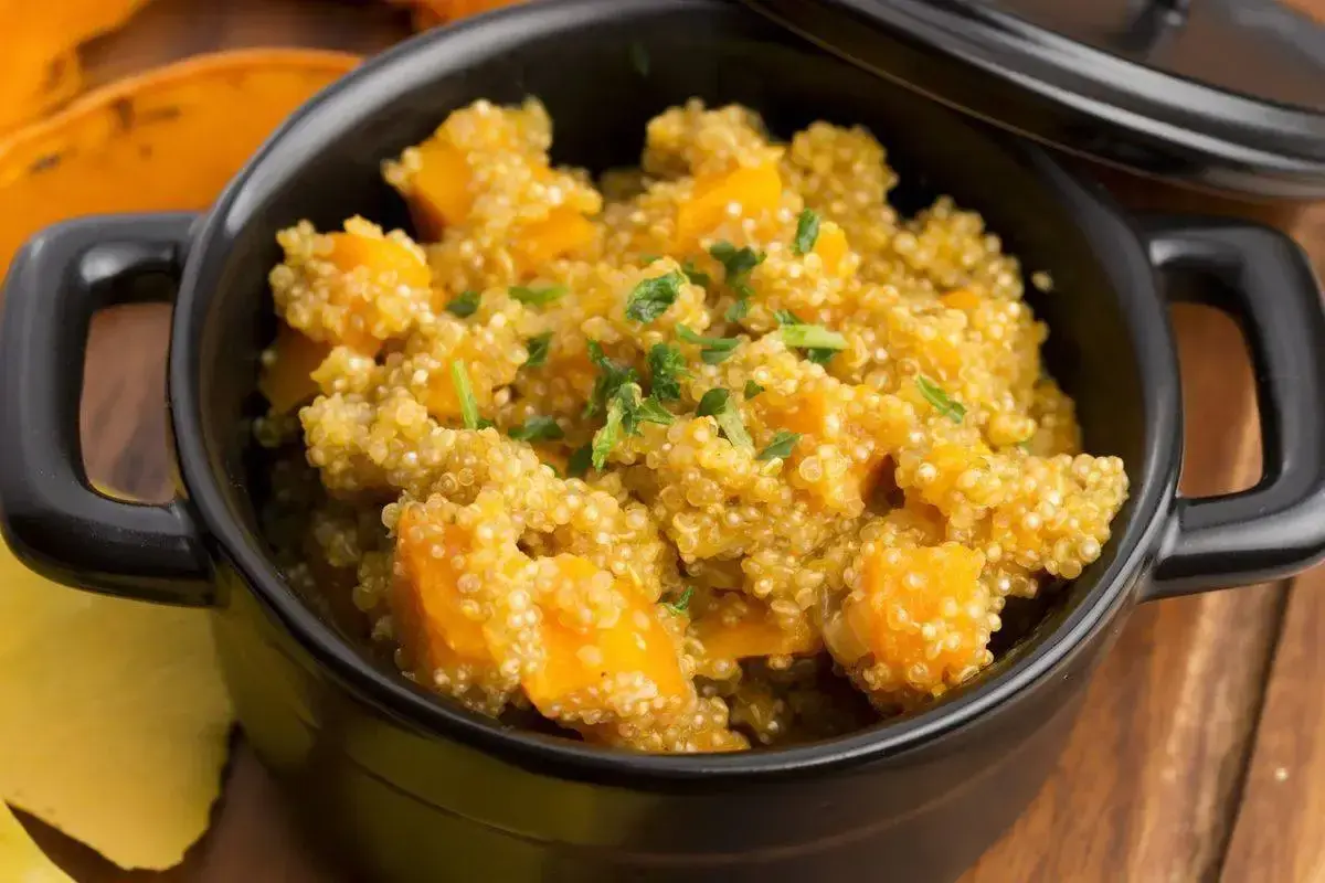 Un saporito piatto di quinoa e zucca, guarnito con erbe fresche, servito in una ciotola nera.