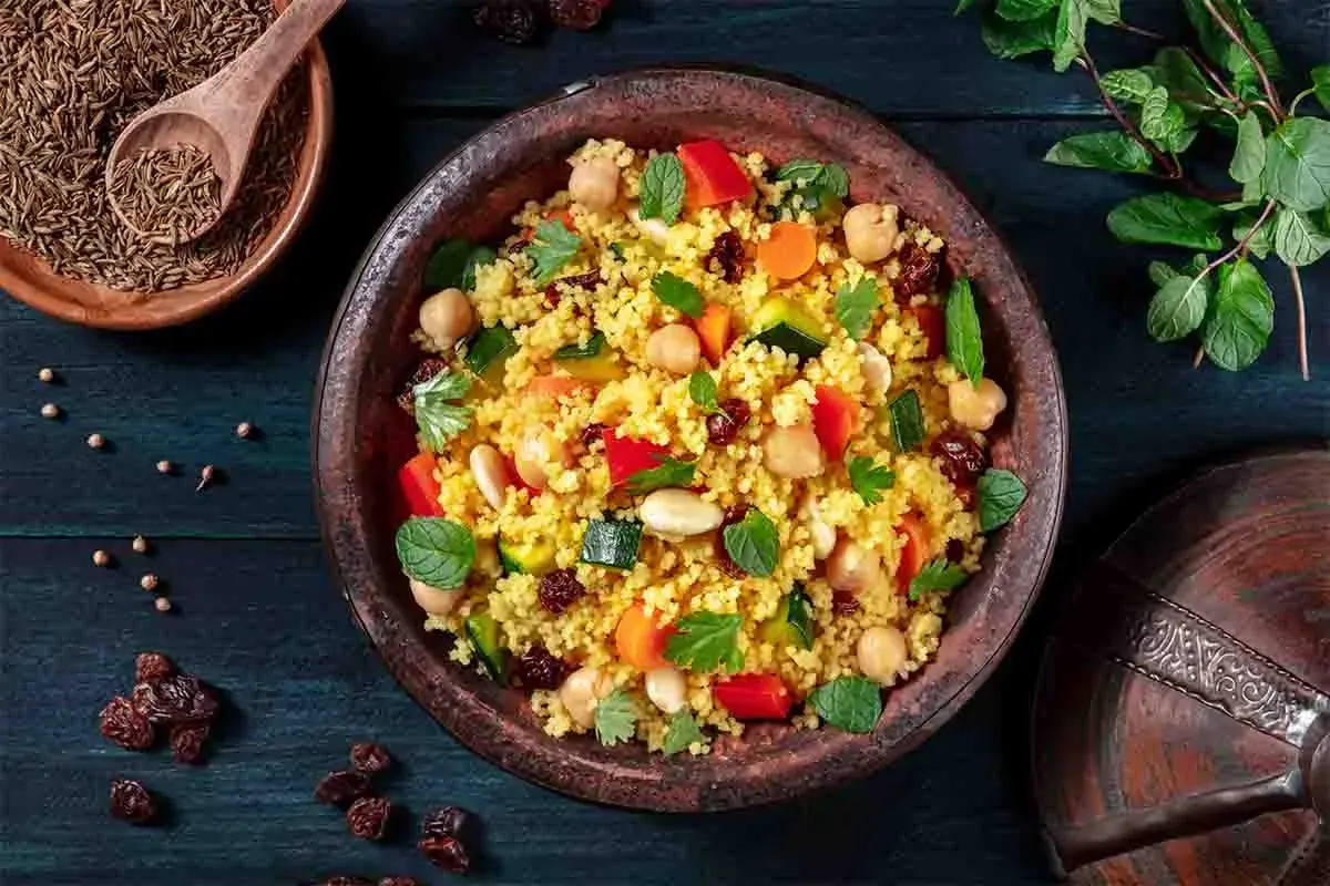 Un piatto colorato di cous cous, con ceci, verdure e uvetta, che evoca le sue antiche origini.