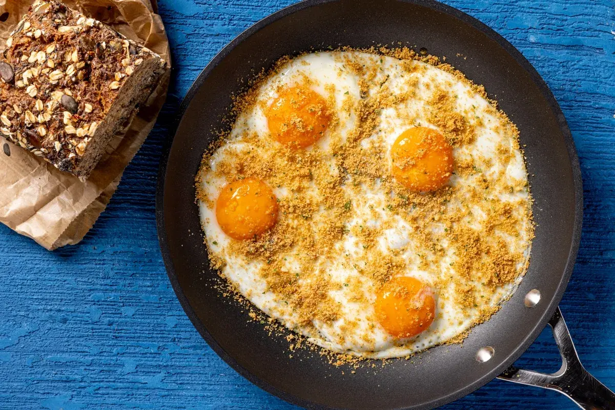 Uova fritte in padella con pangrattato e erbe, accompagnate da pane integrale. Un'idea per ricette fit con uova, sana e gustosa.