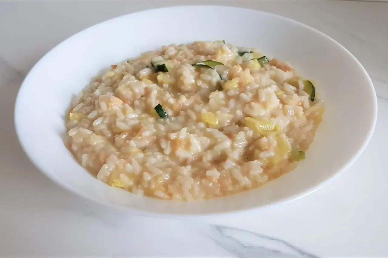 Un cremoso risotto con verdure light, arricchito da zucchine e altri ortaggi freschi, servito in una ciotola bianca.