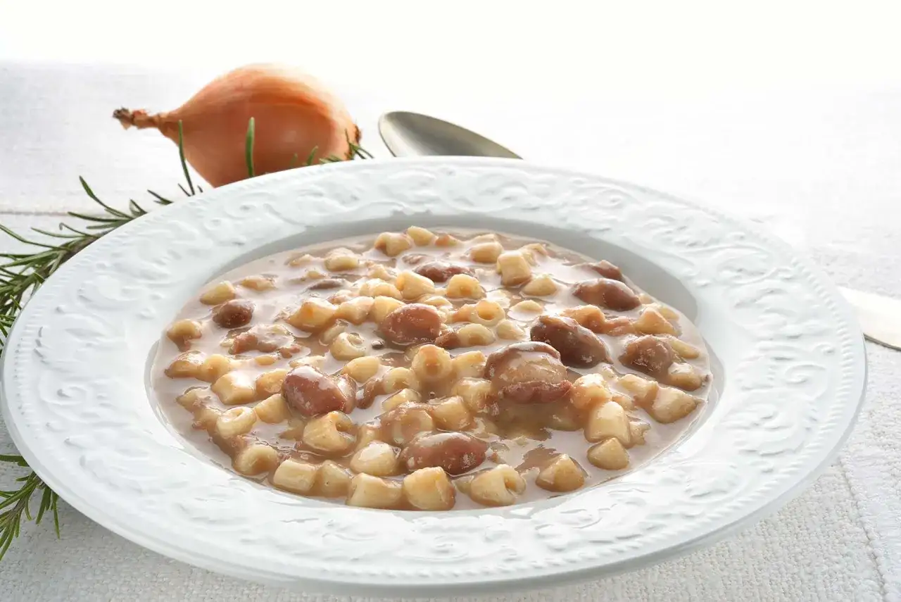 Piatto di pasta e fagioli borlotti, con cipolla e rosmarino sullo sfondo. Un comfort food che scalda il cuore.