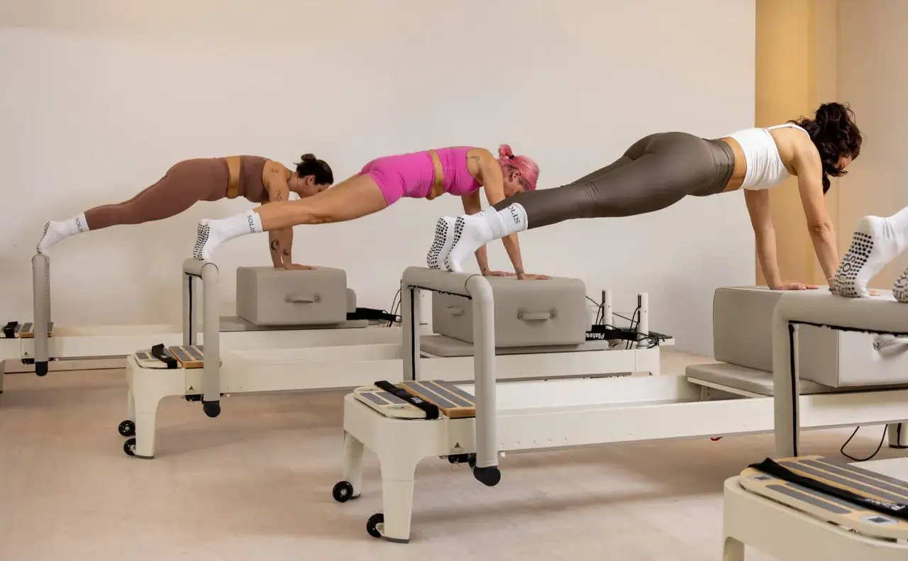 Tre donne eseguono plank sui Reformer Pilates. Un allenamento intenso che offre molti benefici, ma richiede anche impegno.