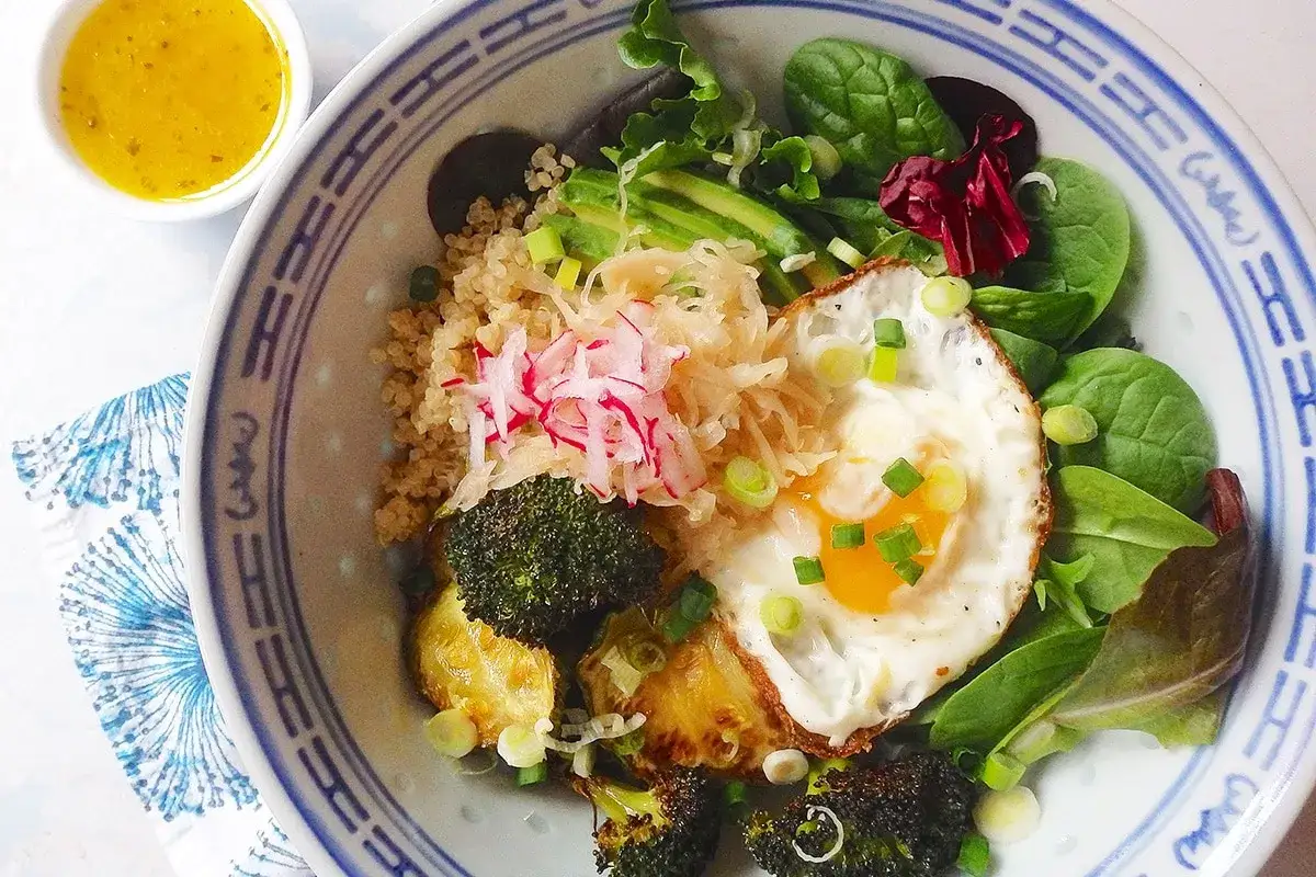 Piatto colorato con quinoa, uovo fritto, broccoli, avocado e verdure. Un'idea su cosa mangiare per la candida, con ingredienti freschi e salutari.