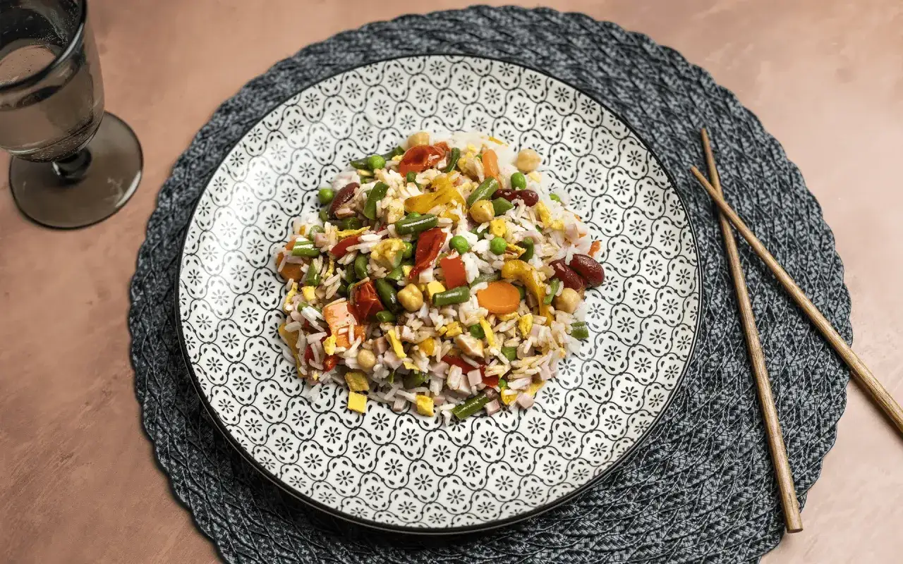 Un piatto di riso saltato con verdure miste, piselli, fagioli, carote e pezzetti di uovo. Un pasto colorato e invitante.
