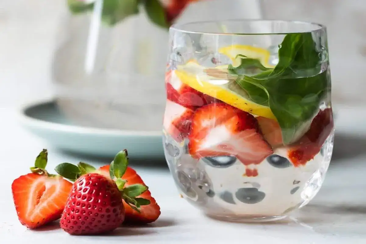 Frullati di frutta con acqua, fragole, limone e foglie verdi in un bicchiere. Fresca bevanda estiva.