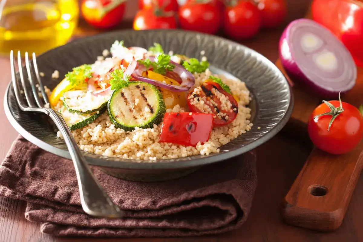 Piatto di cous cous integrale con verdure grigliate (zucchine, pomodori, peperoni, cipolla rossa). Le propriet&agrave; del cous cous integrale lo rendono un pasto sano e gustoso.