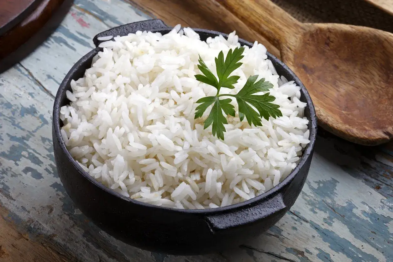 Una ciotola di riso bianco soffice, ideale per chi soffre di colon irritabile, guarnita con prezzemolo fresco.