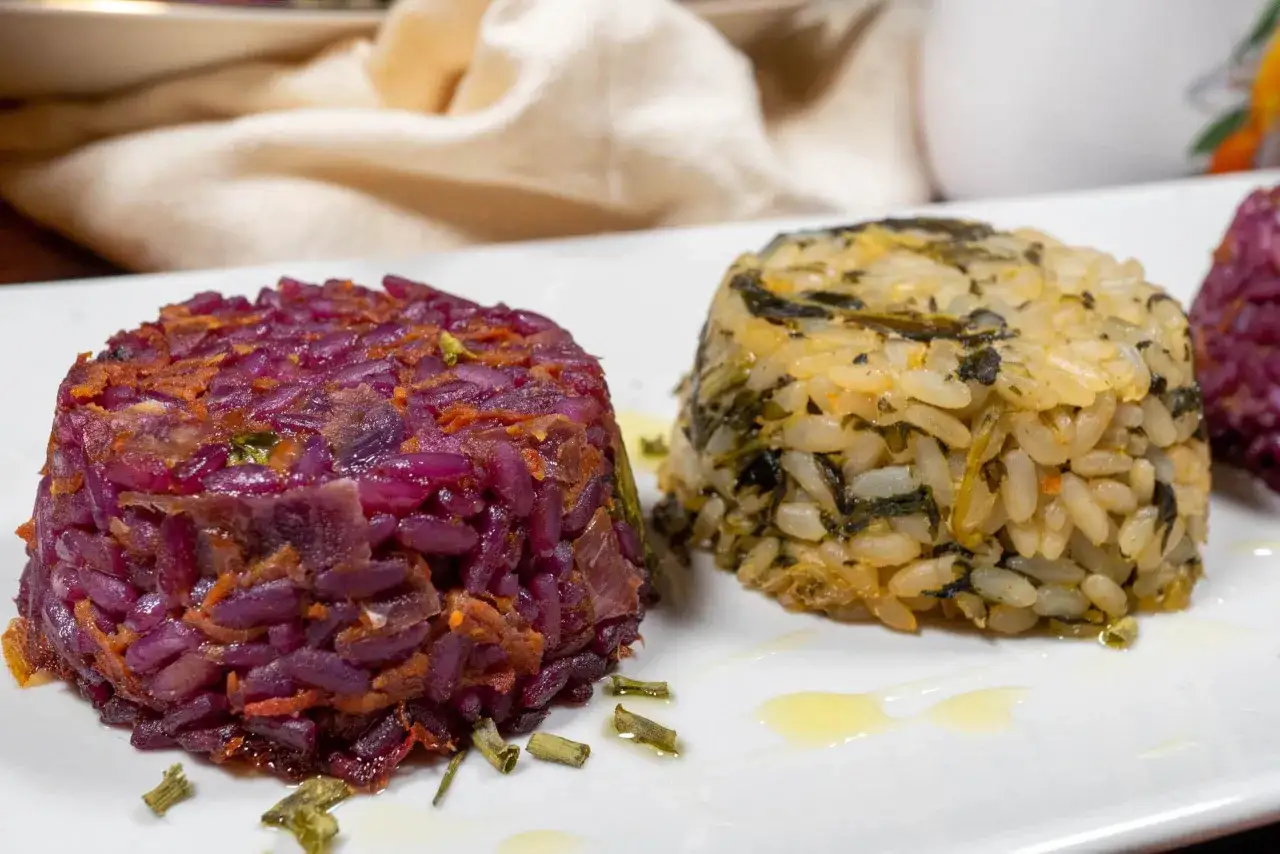 Sformatini di riso e verdure: uno viola intenso, l'altro giallo con verdure verdi, serviti su un piatto bianco con un filo d'olio.