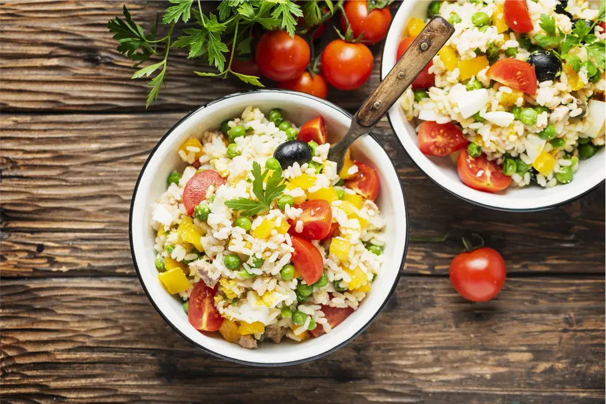 Insalata di riso colorata con pomodorini, piselli, uova e olive. Un'idea fresca su come condire il riso a dieta in modo gustoso e leggero.