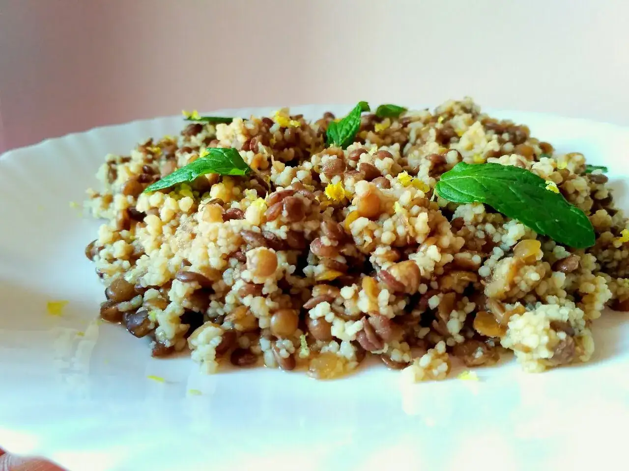 Un saporito cous cous con lenticchie, guarnito con foglie di menta fresca e scorza di limone.