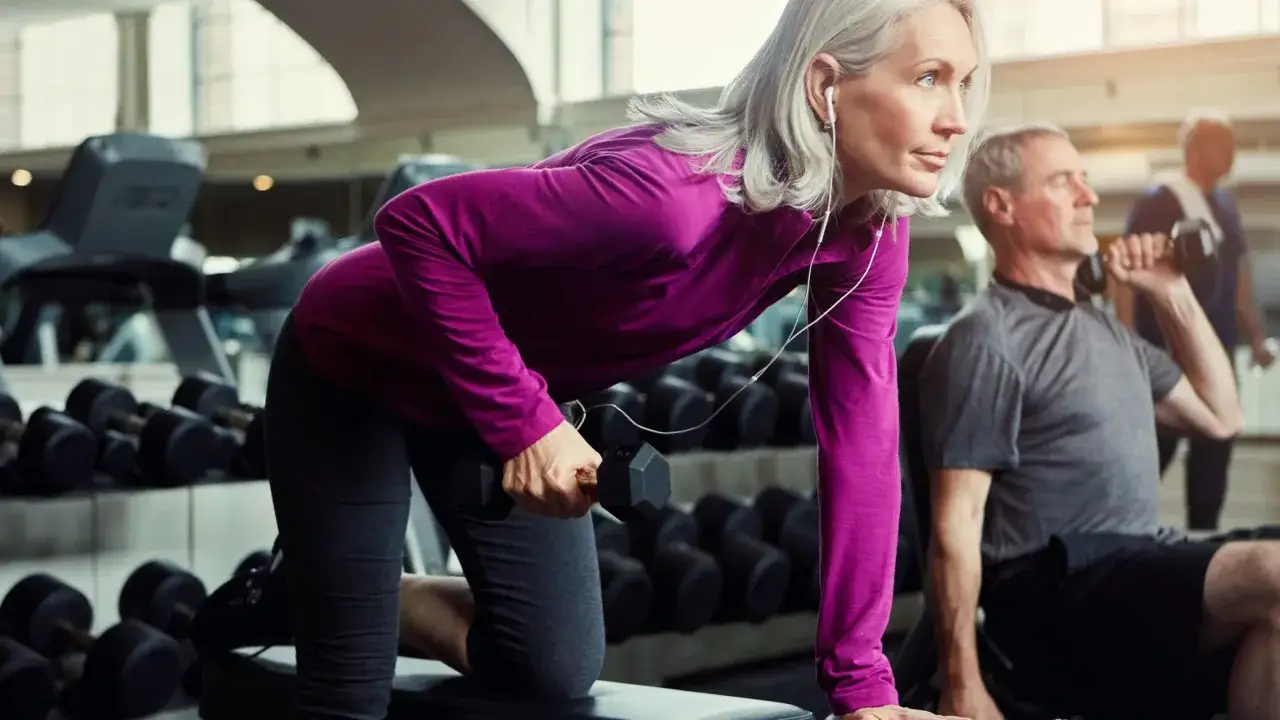 Donna con capelli grigi si allena in palestra con manubri, un esempio di come dimagrire in menopausa con attivit&agrave; fisica.