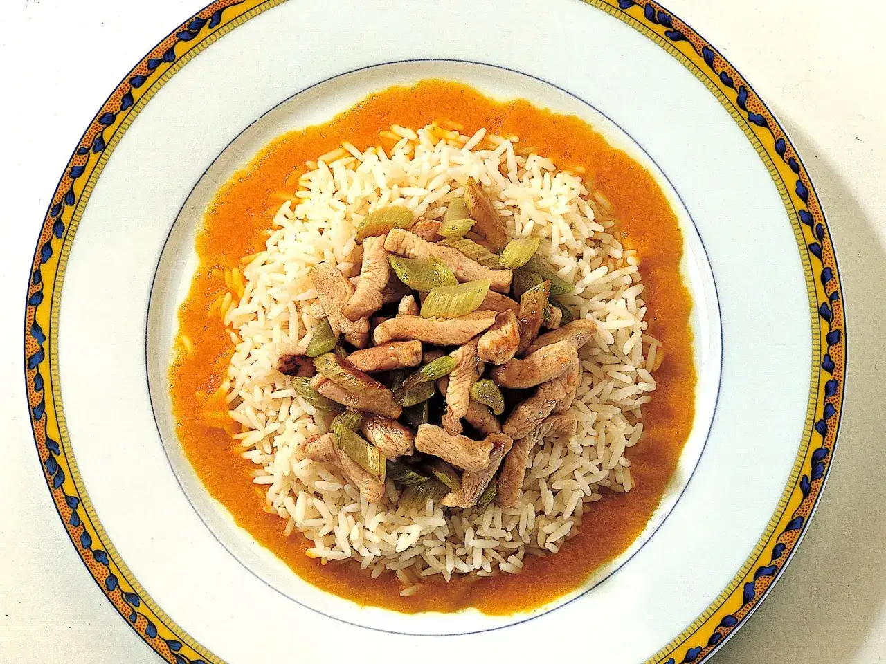 Piatto di riso basmati con zafferano, guarnito con straccetti di pollo e verdure croccanti.