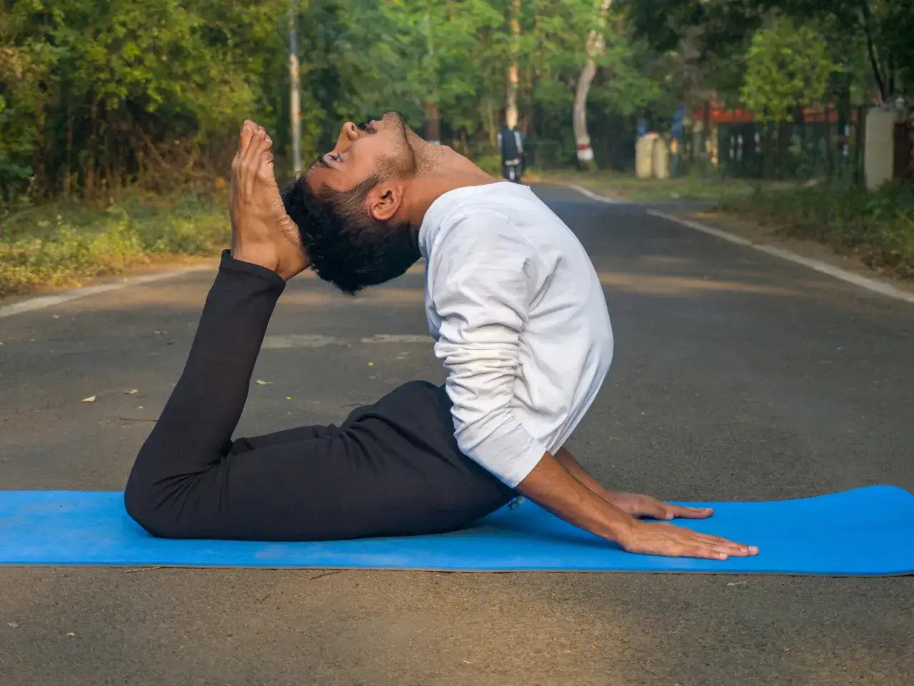 Uomo in posa yoga Dhanurasana su tappetino blu. Un ottimo modo per iniziare con lo yoga, aprendo il petto e rafforzando la schiena.