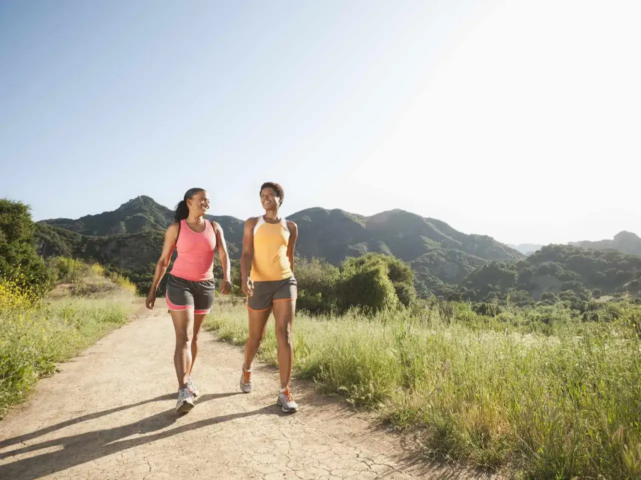 Due donne sorridono mentre fanno una camminata metabolica su un sentiero collinare, godendosi la natura e l'aria fresca.