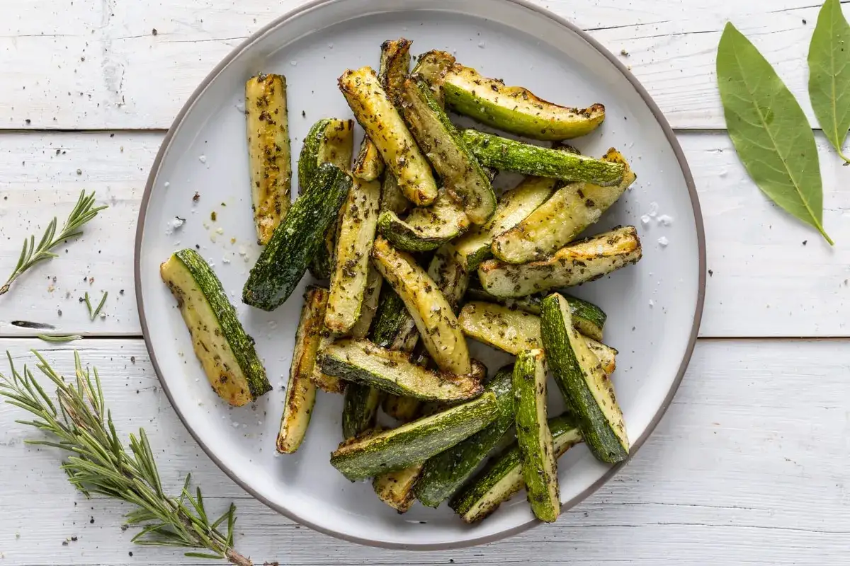 Zucchine e legumi arrostiti, conditi con erbe aromatiche, serviti su un piatto grigio.