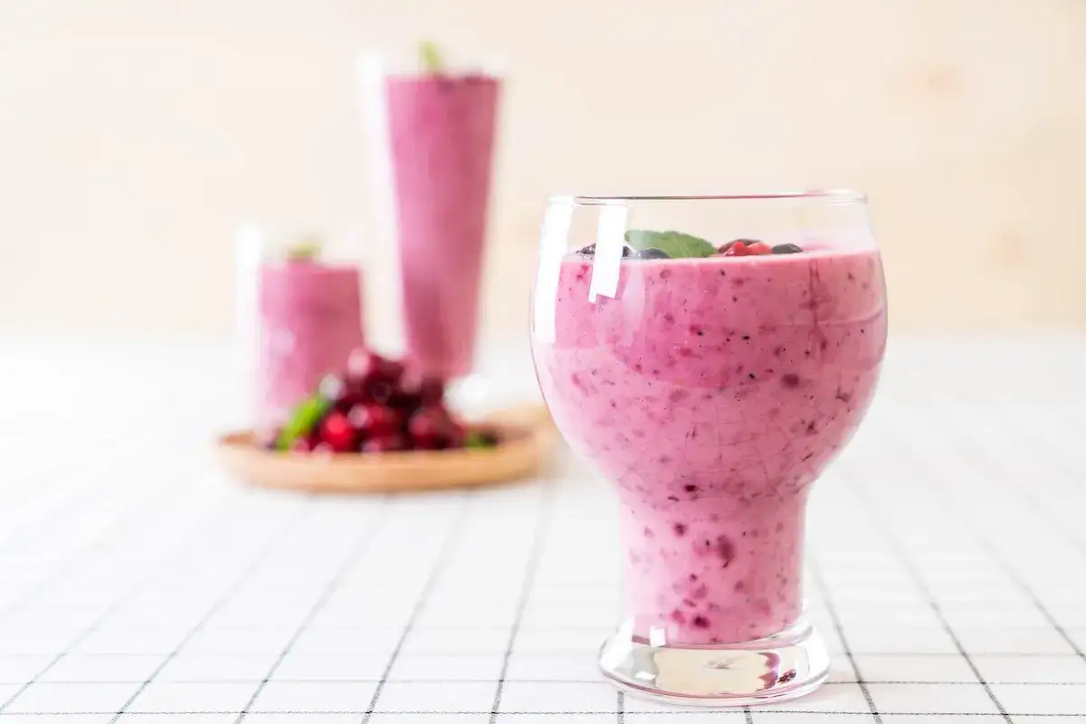 Un cremoso frullato di frutta con latte, guarnito con frutti di bosco freschi e menta, pronto per essere gustato.