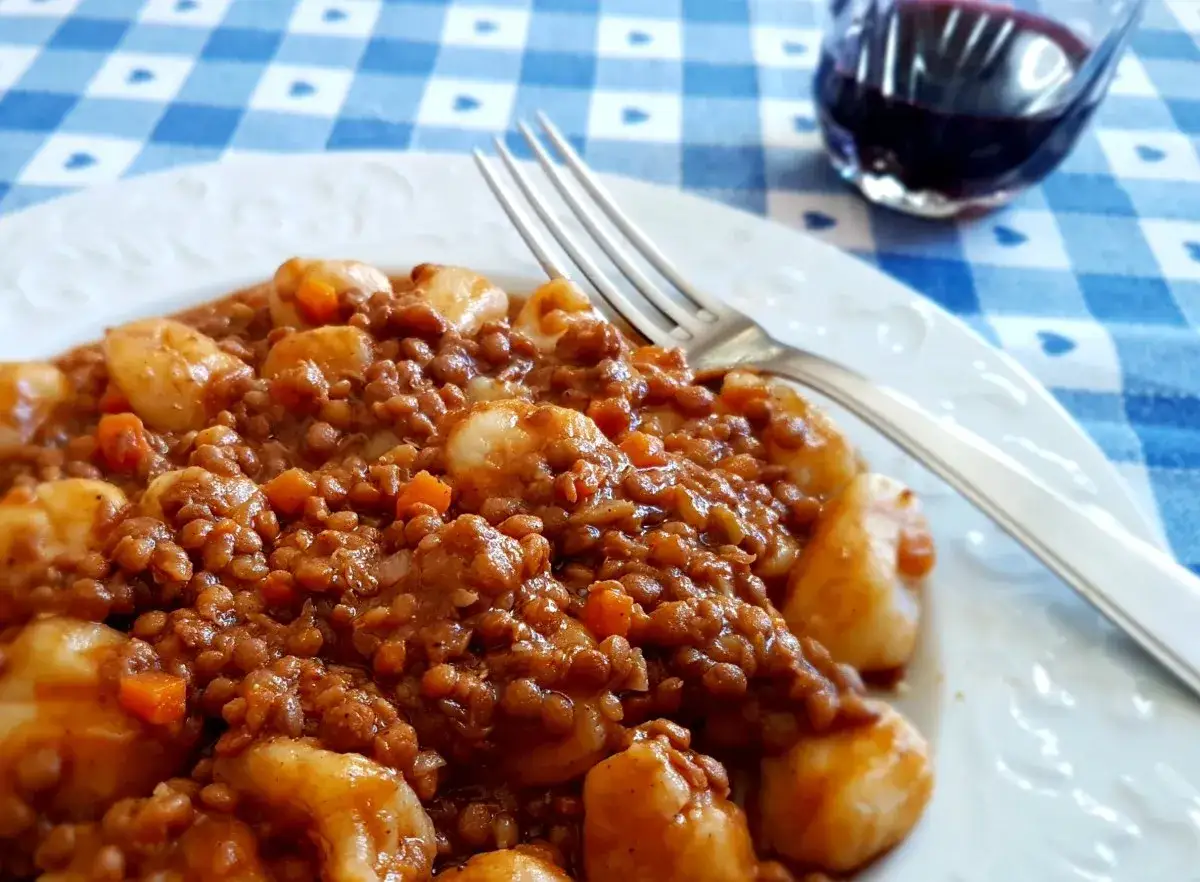 Un piatto di gnocchi e lenticchie, un comfort food gustoso e nutriente, pronto per essere gustato con una forchetta.