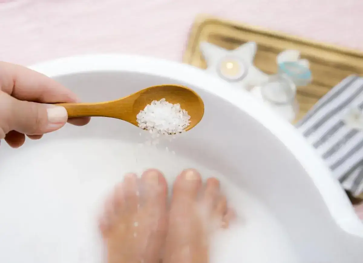Mani aggiungono sale a un pediluvio con acqua e bicarbonato per piedi rilassati.