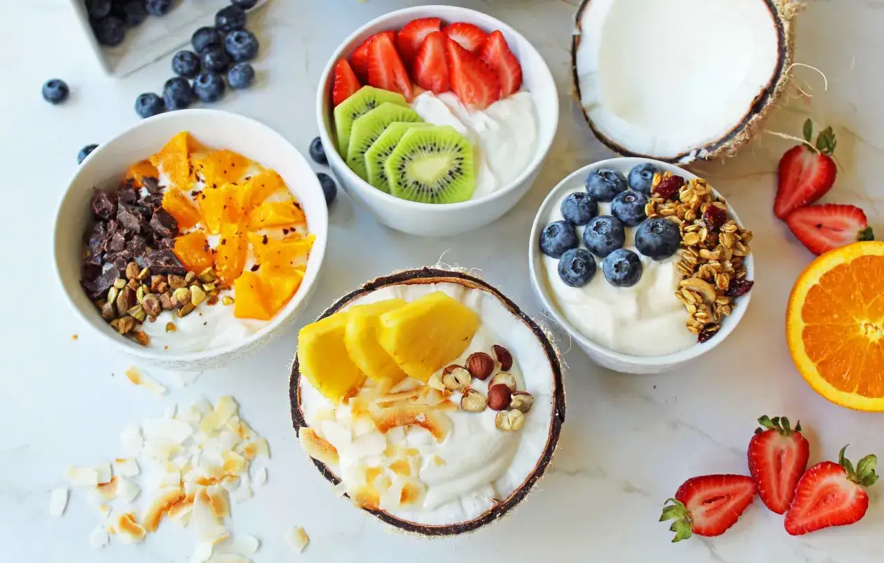 Coppette e mezzo cocco ripiene di yogurt greco, guarnite con frutta fresca, granola e scaglie di cocco.