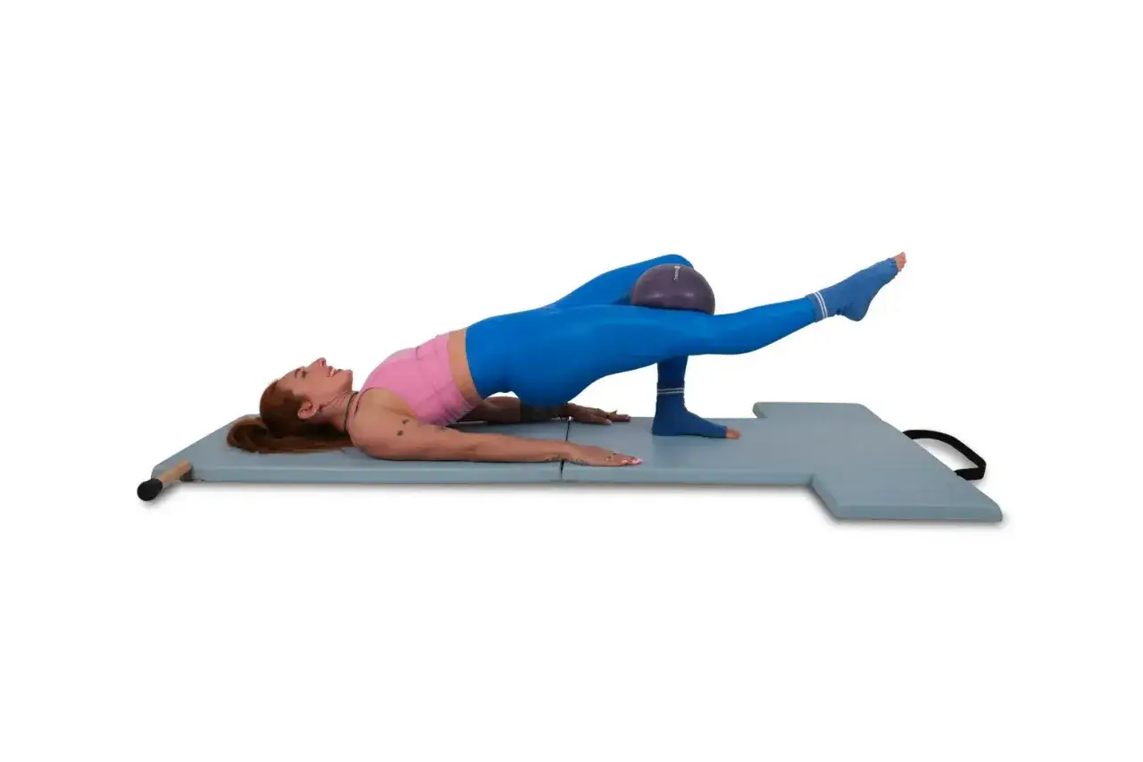 Donna esegue un esercizio di pilates con una softball tra le ginocchia, sollevando un gluteo.