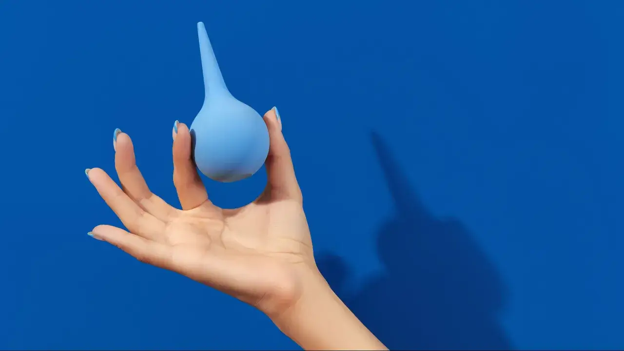 Mano che tiene un clistere con acqua del rubinetto, su sfondo blu.