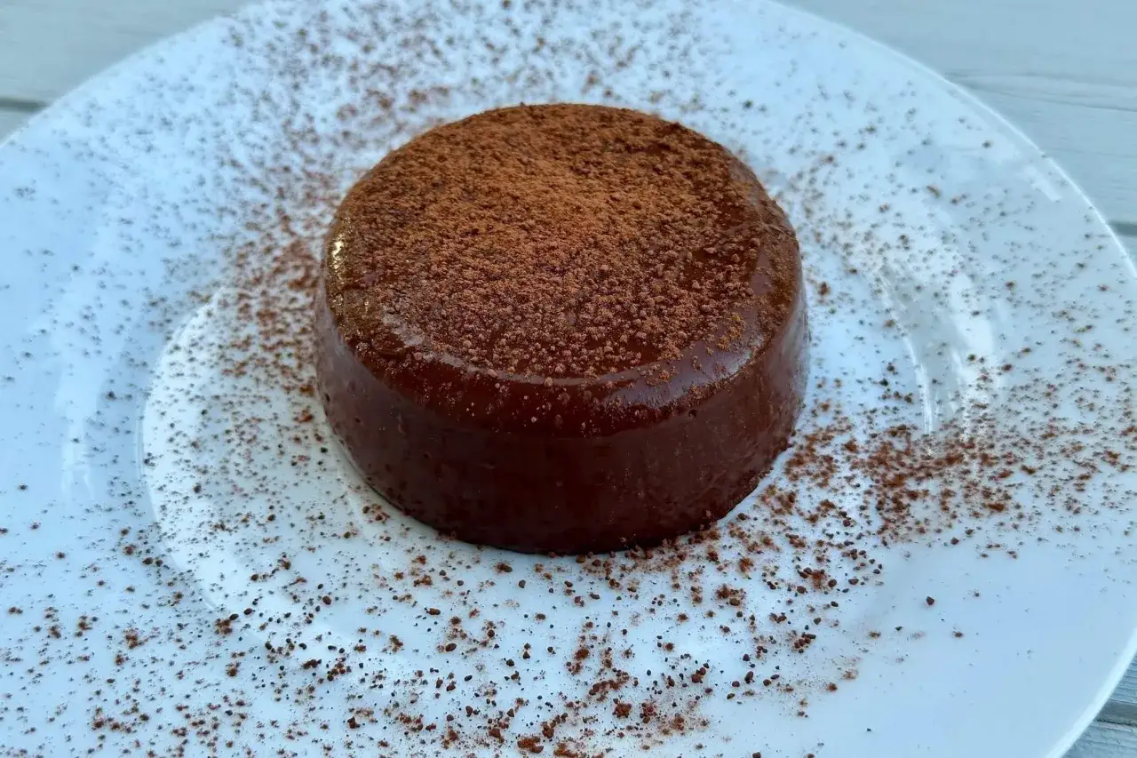 Delizioso budino con cacao amaro, cosparso di polvere di cacao su un piatto bianco.